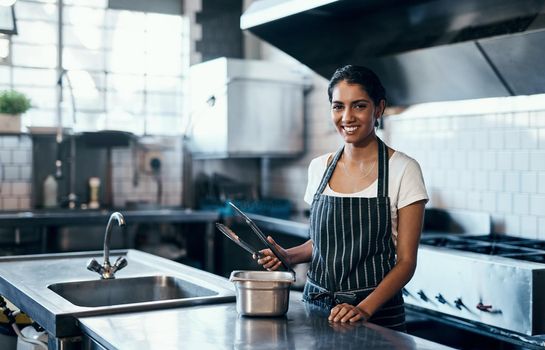 Cooking, making food and working as a chef in a commercial kitchen with tongs and industrial equipment. Portrait of a female cook preparing a meal for lunch, dinner or supper in a restaurant or cafe