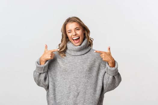 Attractive happy woman in casual clothing pointing at your logo and smiling, winking to encourage you, standing over white background