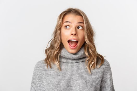 Close-up of amazed blond girl looking at upper left corner, standing surprised over white background