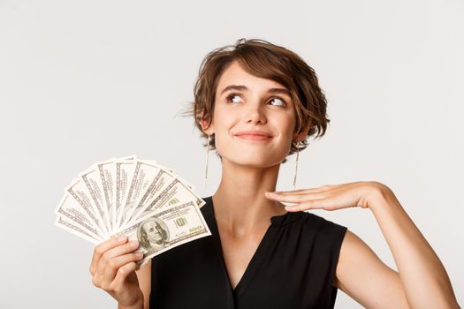 Fashionable rich elegant woman looking sassy, showing money, standing over white background