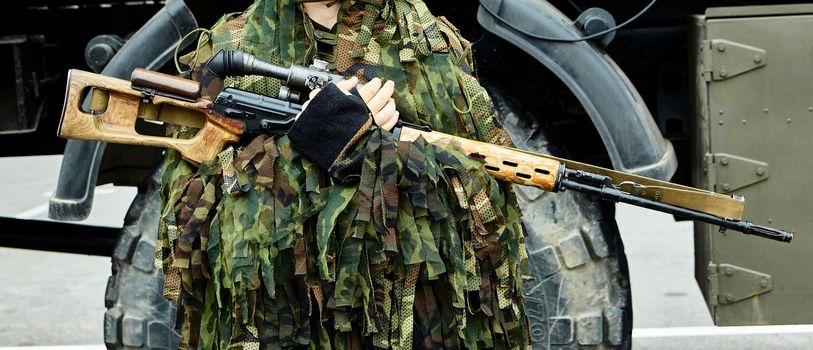 Close-up portrait of a military sniper in camouflage green army clothes with a Degtyarev sniper rifle in his hand.