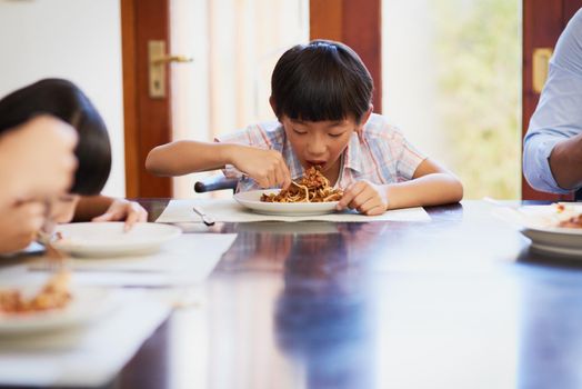 He just couldnt wait to dig in to his favourite meal. a little boy enjoying a meal with his family at home.
