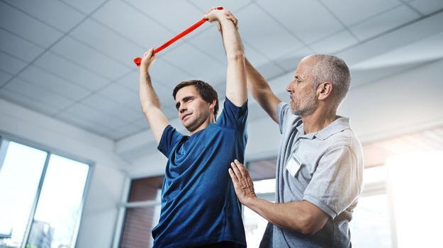 Theres no reason to make your injuries an impediment. a physiotherapist helping a patient stretch with resistance bands.