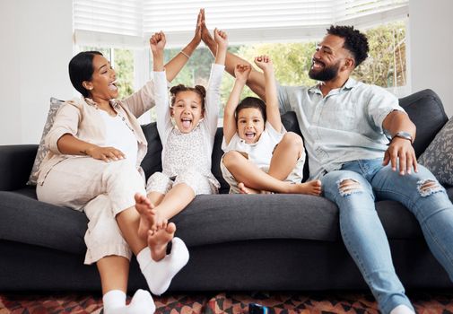 Happy parents and excited children celebrate on the sofa while watching tv. Fun family time, relaxing at home and bonding. Mother and father high five, kids cheer for sports team win.