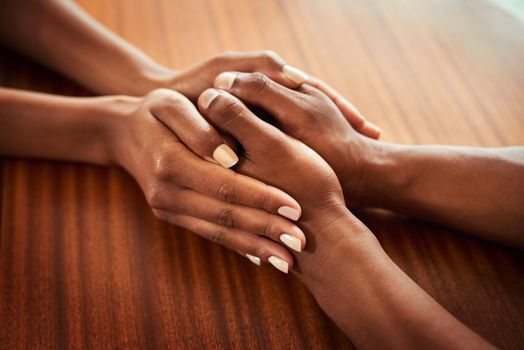 You dont have to go through this alone. Closeup of two unrecognizable peoples hands holding each other while resting on top of a wooden table.