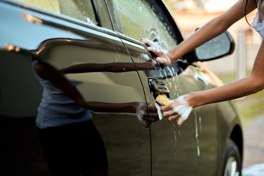 Paying attention to detail. an unrecognizable young child washing their parents car outside during the day.
