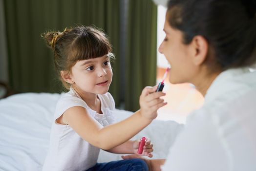 Shes a little makeup artist in the making. a mother and her little daughter playing with makeup on the bed at home.