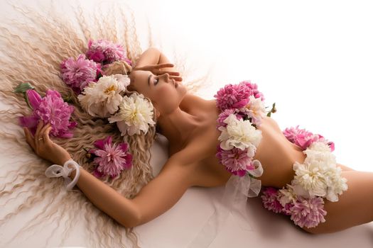 Sensual naked lady with flowers on body lying on bed