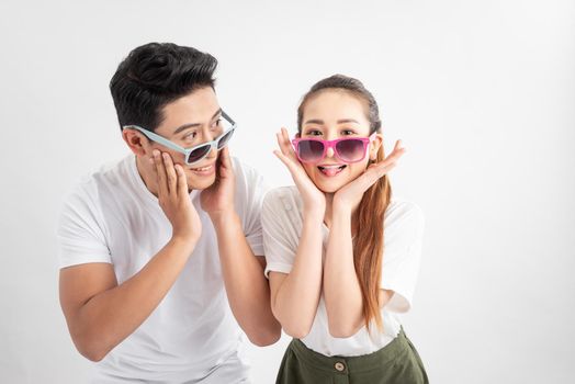 Funny couple  touches cheeks with both hands in casual style clothes and color glasses over white background