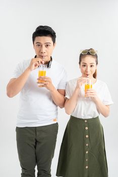 Stylish couple in casual clothes is drinking juice, looking at camera and smiling on white background