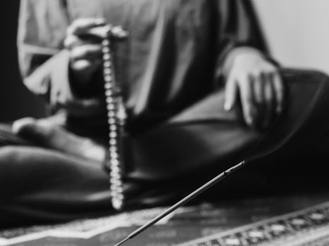 Concentrated woman praying with wooden rosary mala beads. Close up, focus on incense stick. Black and white