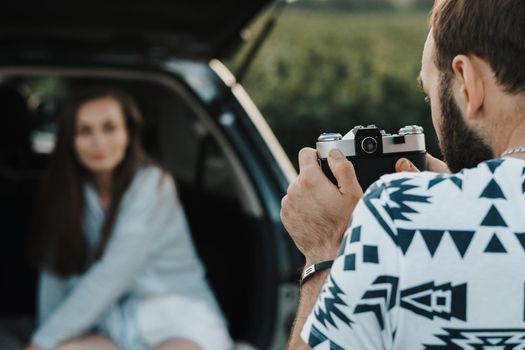 Man using old film camera to photography his girlfriend who sitting inside trunk of SUV car