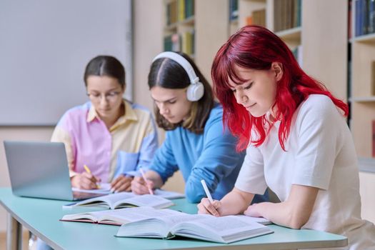 Group of teenage students study at their desks in library class