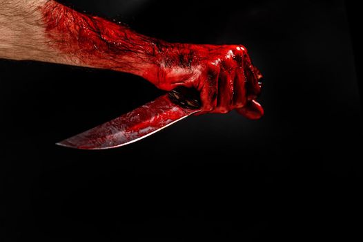 Man holding knife with bloody hand on black background.
