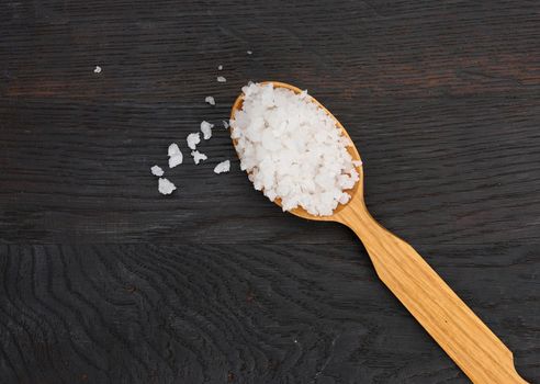 Large crystals of white sea salt in a brown wooden spoon