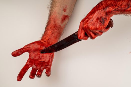 A man with bloody hands cuts himself with a knife.