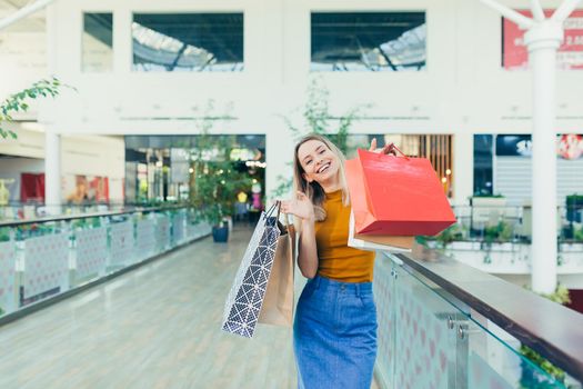 cheerful young shopaholic woman holding paper bags with purchases and smiling