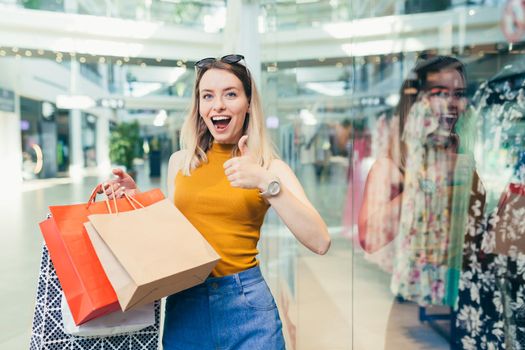 cheerful young shopaholic woman holding paper bags with purchases and smiling
