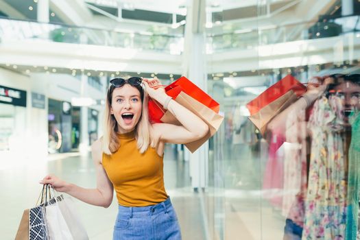 cheerful young shopaholic woman holding paper bags with purchases and smiling l