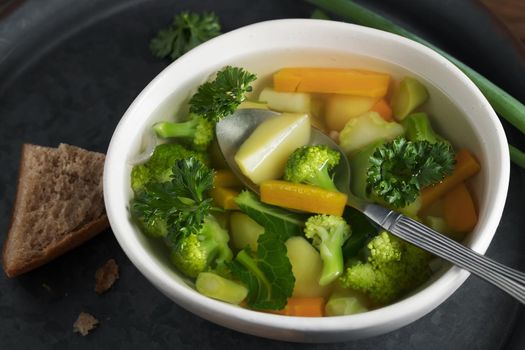 Vegetarian vegetable soup with carrots, broccoli and parsley in a light bowl on a metal tray on a wooden table