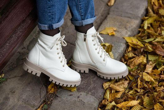 Female legs in a jeans and white fashion boots with laces. fallen leaves on the sidewalk
