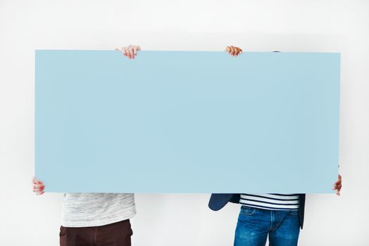 Backed by the boys themselves. Studio shot of two men covering themselves with a blank placard against a white background.