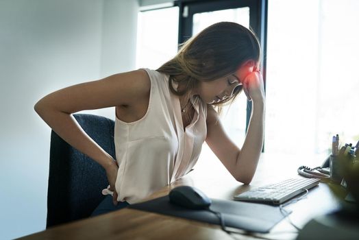 Feeling the pain all around her body. a young businesswoman suffering from a headache and back pain while working in an office.