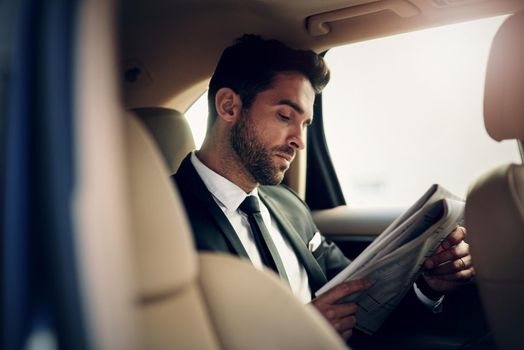 Reading newspaper early in the morning. a confident young businessman reading the newspaper while being seated in the backseat of a car.