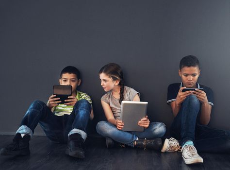 Tweens and their screens. Studio shot of kids sitting on the floor and using wireless technology against a gray background.