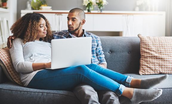 Technology keeps modern couples connected. a young couple relaxing on the sofa at home and using a laptop together.
