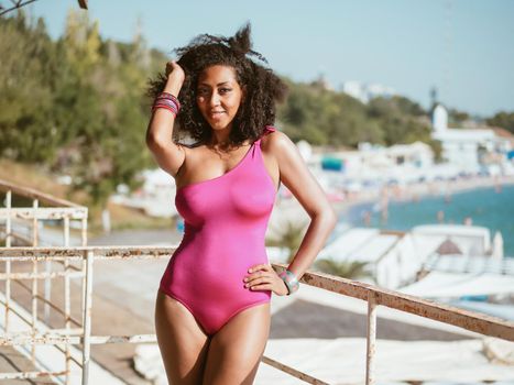 Portrait of cheerful black people, pretty happy young afro american woman smiling on sea beach. Sexy girl in pink swimsuit and jewelry enjoying nature.Lady wearing bikini.