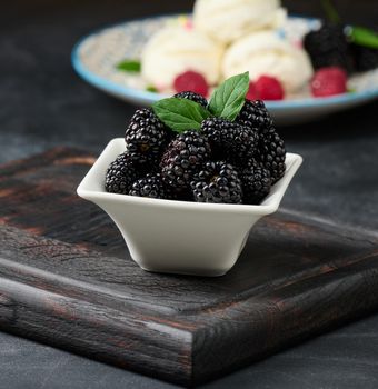 A bunch of ripe blackberries in a white ceramic plate on a black table