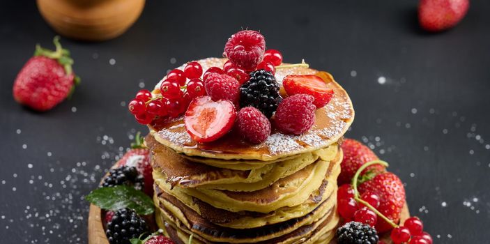 A stack of pancakes with fresh fruits poured with syrup on a black background