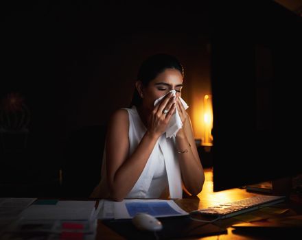 Its not a productive condition to work in. a young businesswoman blowing her nose while working late in an office.