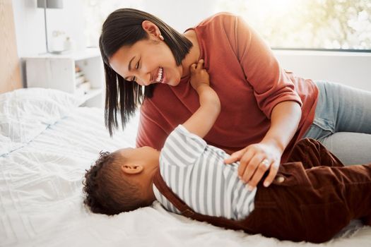 Happy, loving family with a mother and son being playful and bonding on a bed at home. Smiling parent playing with her child, laughing and enjoying motherhood. Single parent embracing her son