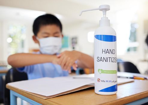Boy rubbing hand sanitizer for hygiene, safety and protection against covid at school. Closeup bottle of alcohol gel on desk in classroom to clean, kill or prevent the spread of germs or coronavirus