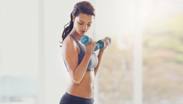Working on her upper body. an attractive young woman working out with dumbbells in her home.