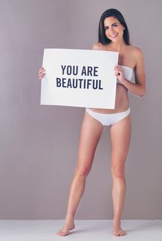 Just sending you a reminder to say...Studio portrait of an attractive young woman holding a sign that reads you are beautiful against a pink background.