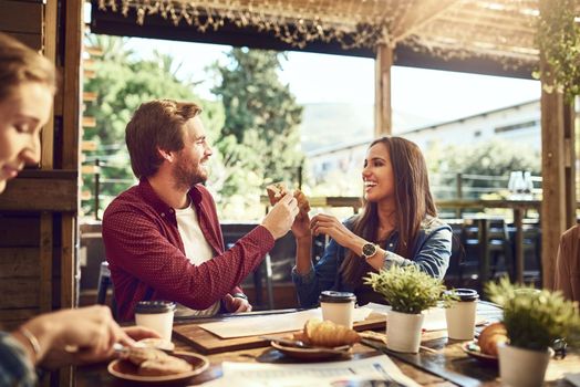Cheers to good food and good looking people. an affectionate young couple toasting with sandwiches while enjoying themselves at lunch.