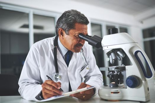 Medical mysteries uncovered. a mature scientist using a microscope and recording his findings in a laboratory.