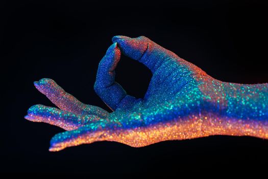 Jnana Gian mudra - Om on black background. Female hand covered with holographic shining glitter under neon colored