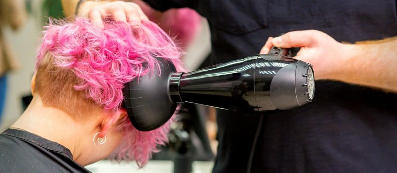 Hairdresser drying short pink hair