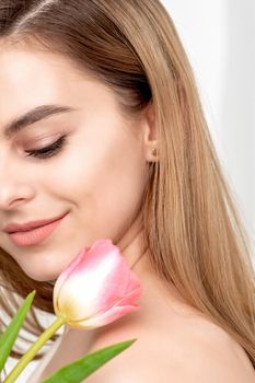 A portrait of a happy young caucasian woman with closed eyes and one pink tulip against a white background with copy space