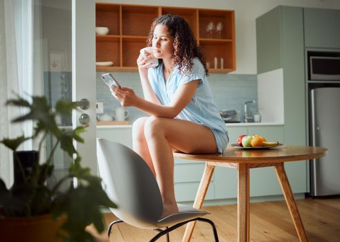 Woman browsing social media on phone, drinking cup of coffee and relaxing in the morning at home. Relaxed, content and serious female browsing the internet, posting on status online and chatting