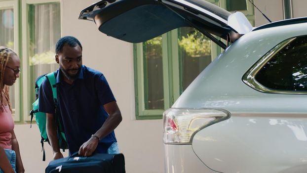Positive african american couple putting voyage luggage inside car trunk
