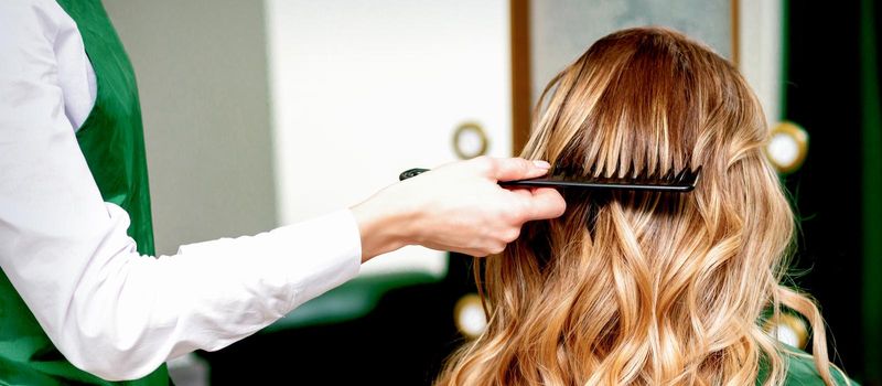 Hairdresser combing wavy hair of woman