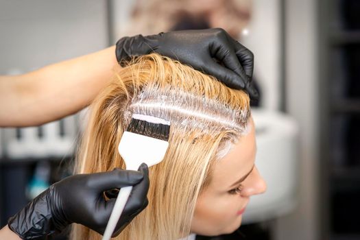 Hairdresser dyeing blonde hair roots