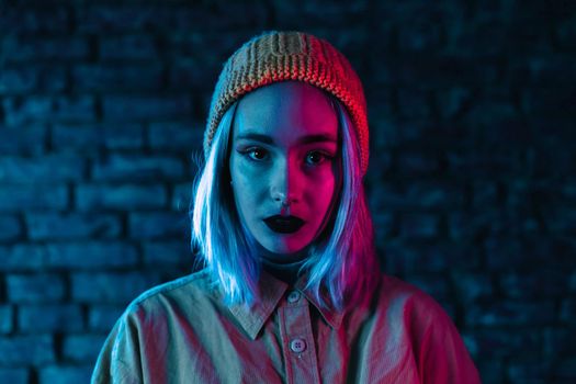 Young woman in pink and blue neon light. Portrait of unusual beautiful punk girl with colorful hairstyle on bricks wall studio background
