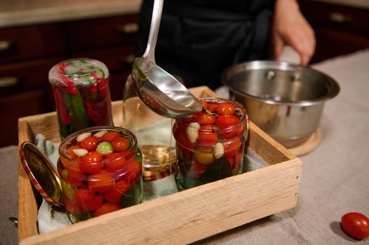Pouring boiling marinade into jars with cherry tomatoes. Canning. Preparing homemade fermented vegetable. Close-up