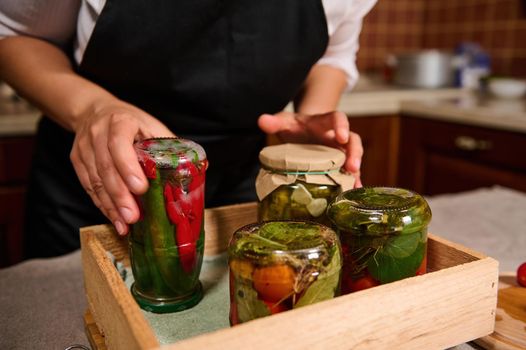 Close-up. Housewife putting jar with fermented hot chili upside down on a wooden crate with homemade preserves